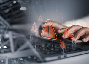 Hands on a keyboard with digital warning symbols, used as a stock image to represent IT security risks