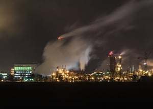 An energy company's illuminated refinery at night, with steam rising